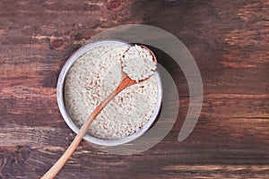 A bowl of uncooked rice on the wooden table, top view.