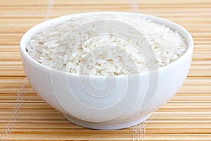 Bowl of uncooked white long grain rice on a bamboo mat