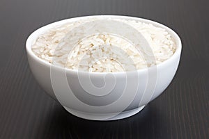 Bowl of uncooked white long grain rice on dark table