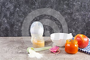 Bowl with vegetables puree and bottle of baby food on gray background