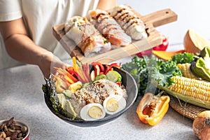 Bowl with vegetables and rice and spring rolls in female hands in the kitchen.