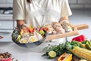 Bowl with vegetables and rice and spring rolls in female hands in the kitchen.