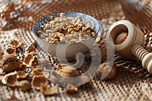 A bowl of walnuts placed on a table with shells and a wooden nutcracker lying around in a rustic style