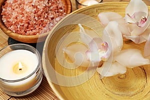Bowl with water, flowers, sea salt and burning candles on bamboo mat, closeup. Spa treatment