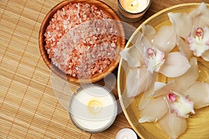 Bowl with water, flowers, sea salt and burning candles on bamboo mat, flat lay. Spa treatment