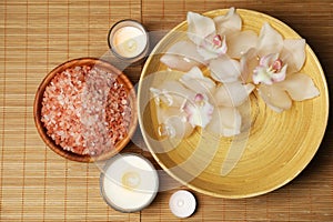 Bowl with water, flowers, sea salt and burning candles on bamboo mat, flat lay. Spa treatment