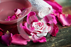 Bowl with water and rose petals on wooden table