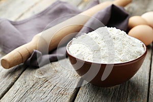 Bowl of wheat flour with eggs and rolling pin on grey wooden background