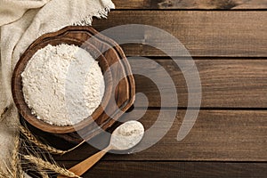 Bowl with wheat flour, spoon and spikelets on wooden table, flat lay