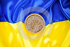 Bowl with wheat grains on the background of the flag of Ukraine. Concept of food supply crisis and global food scarcity because of