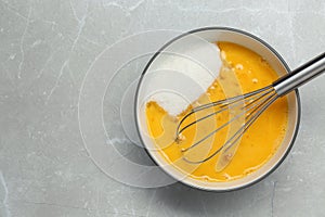 Bowl with whisked eggs and sugar on grey table, top view. Space for text photo