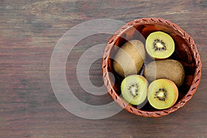 Bowl of whole and cut fresh kiwis on wooden table, top view. Space for text