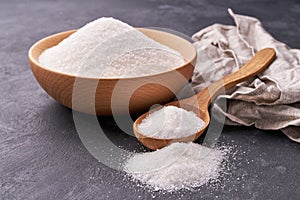 Bowl and wooden spoon full of white sugar on black background