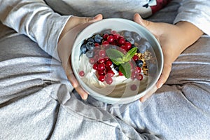 A bowl with yogurt, granola, blueberries and cranberries in the hands of a child, healthy breakfast concept.