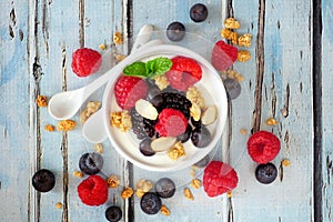 Bowl of yogurt with healthy fresh berries and granola, close up top view over blue wood