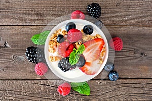 Bowl of yogurt with healthy fresh berries and granola, close up top view over rustic wood