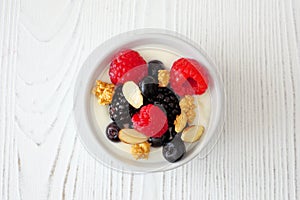 Bowl of yogurt with healthy fresh berries and granola, close up top view on white wood