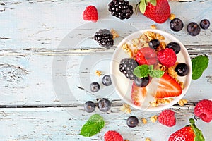 Bowl of yogurt with healthy fresh berries and granola, top view with ingredients on a blue wood background