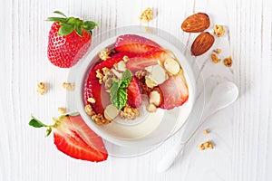 Bowl of yogurt with healthy strawberries and granola, close up top view on a white wood background
