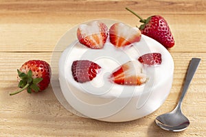 Bowl of yogurt and red fruit strawberry on the wood table. Yogurt made from milk fermented by added bacteria, often sweetened and