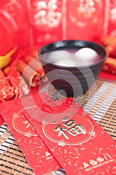 A bowl of Yuanxiao and hongbao in red background. The Chinese characters in the picture mean `happiness` and `good luck`