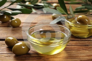 Bowls with cooking oil and olives on wooden table, closeup