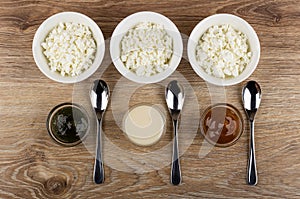 Bowls with cottage cheese, bowls with jam, condensed milk, boiled condensed milk and spoons on table. Top view