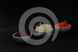 Bowls of cut vegetables - beet, cabbagee, carrot isolated on black background