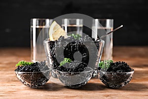 Bowls with delicious black caviar on wooden table
