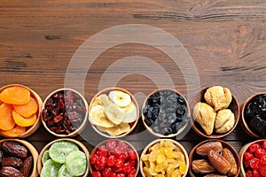 Bowls of different dried fruits on wooden background, top view with space for text