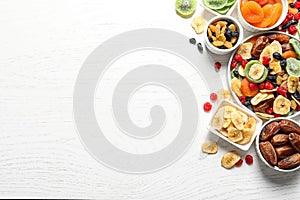 Bowls of different dried fruits on wooden background, top view with space for text