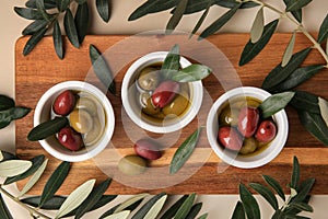 Bowls with different ripe olives and leaves on beige background, flat lay