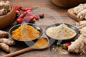 Bowls of ginger and curcuma ground to powder. Red chilli pepper pods, whole ginger and turmeric roots on kitchen table.