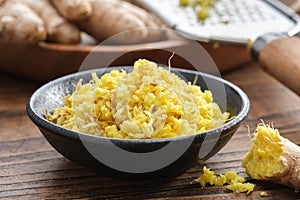 Bowls of grated fresh ginger roots. Whole ginger roots and grater on background. Healthy food.