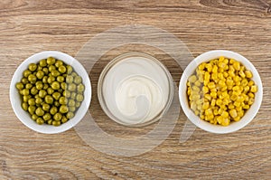 Bowls with green peas, sweet corn and mayonnaise on table