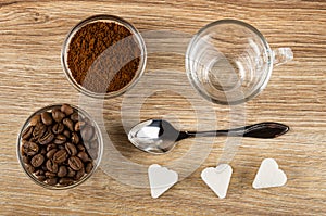 Bowls with ground coffee, coffee beans, empty cup, spoon, pieces of sugar on wooden table. Top view
