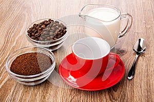 Bowls with ground coffee and coffee beans, spoon, cup on saucer on table