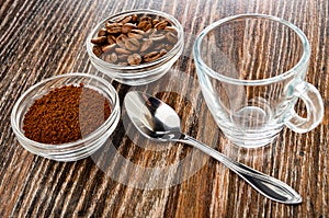 Bowls with ground coffee and roasted coffee beans, spoon, coffee cup on wooden table