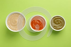 Bowls with healthy baby food on light green background, flat lay