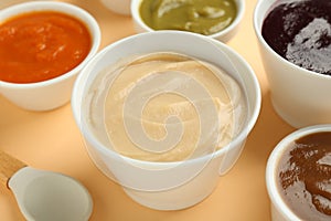 Bowls with healthy baby food and spoon on pale orange background, closeup