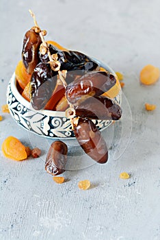 Bowls with juicy dates on a branch and dried apricots on a gray-blue background. Healthy tasty food