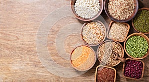 Bowls of legumes, lentils, chickpeas, beans, rice and cereals on wooden background