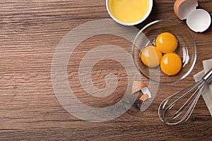 Bowls with raw egg yolks and white on wooden table, flat lay. Space for text