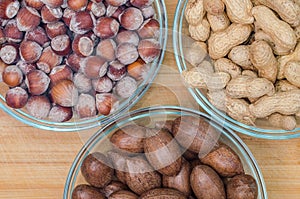 Bowls of raw hazelnuts and pecan nuts on a wooden background. Oleaginous
