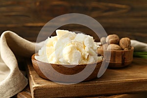 Bowls with shea butter and nuts on wooden background, closeup