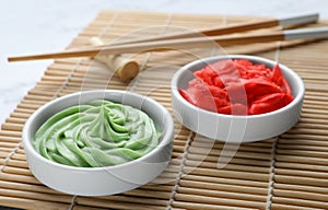 Bowls with swirl of wasabi paste and pickled ginger on bamboo mat, closeup