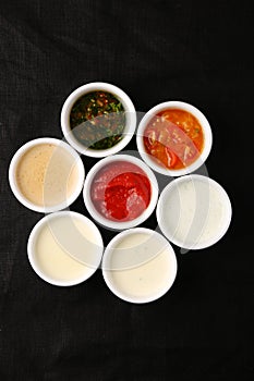 Bowls of various sauces on black background
