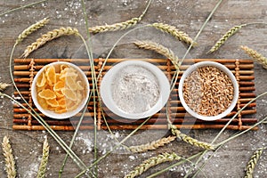 Bowls with wheat flour, grains and pasta on wooden table