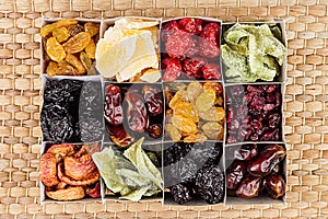 Box with assortment of dried fruits closeup on beige mat background.