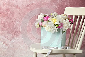 Box with beautiful flowers on wooden chair against color background